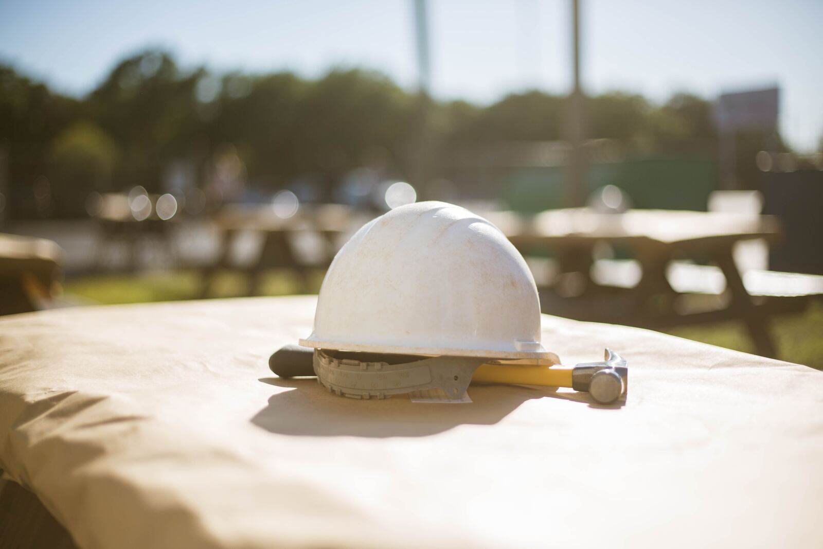 Un casque de chantier et un marteau posés sur une table, au soleil, sur un chantier.