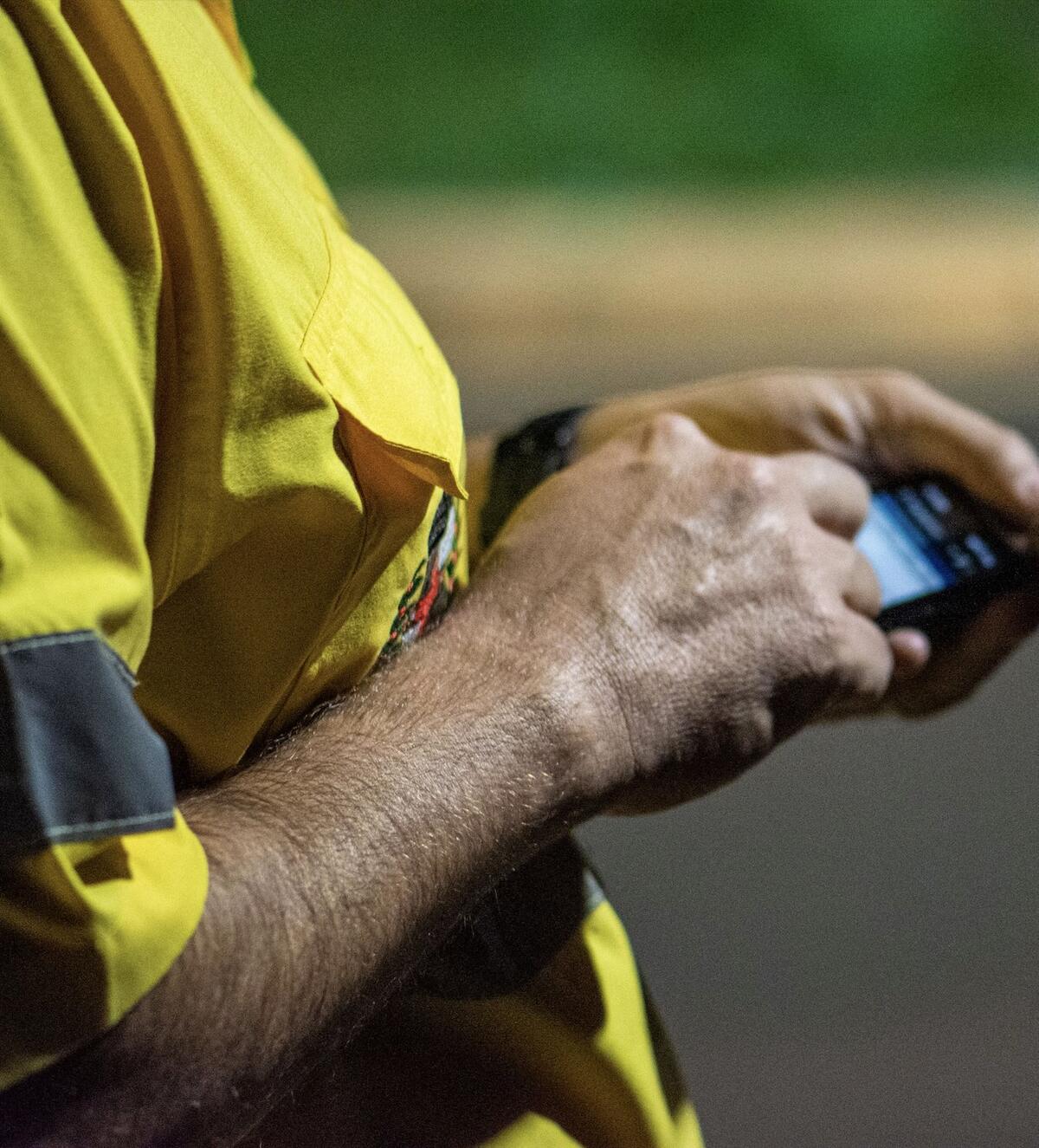 Les mains d'un artisan en gilet haute visibilité tapent sur un téléphone.